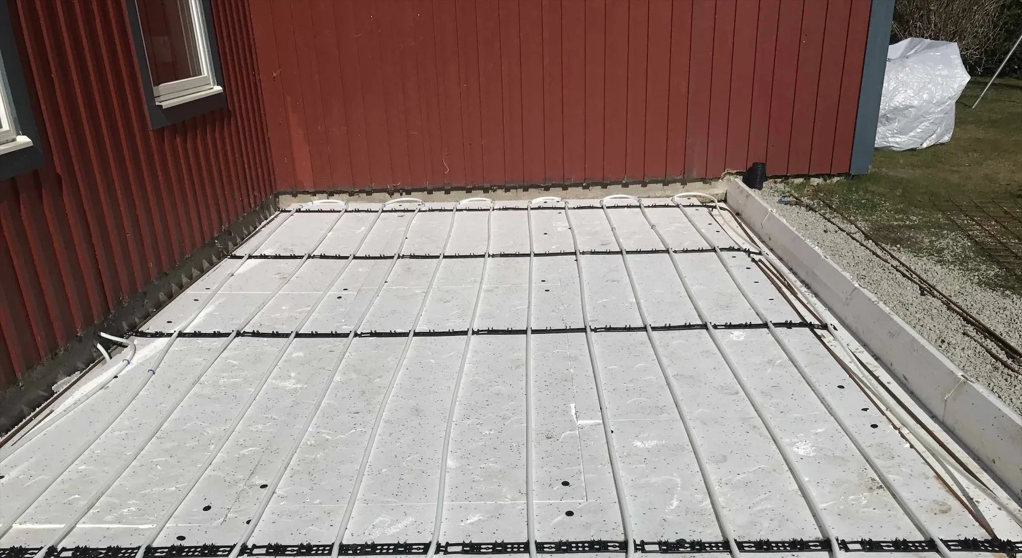 Betongplatta med golvvärmeslingor till ett uterum vid ett rött hus