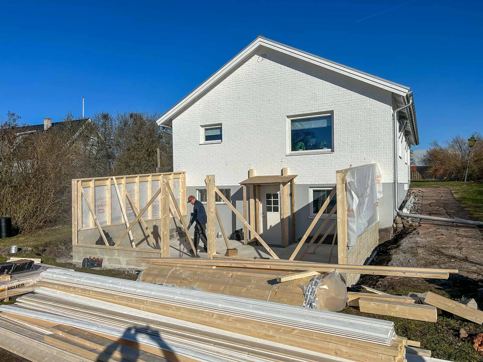 Stommen till en tillbyggnad mot ett vitt hus under blå himmel