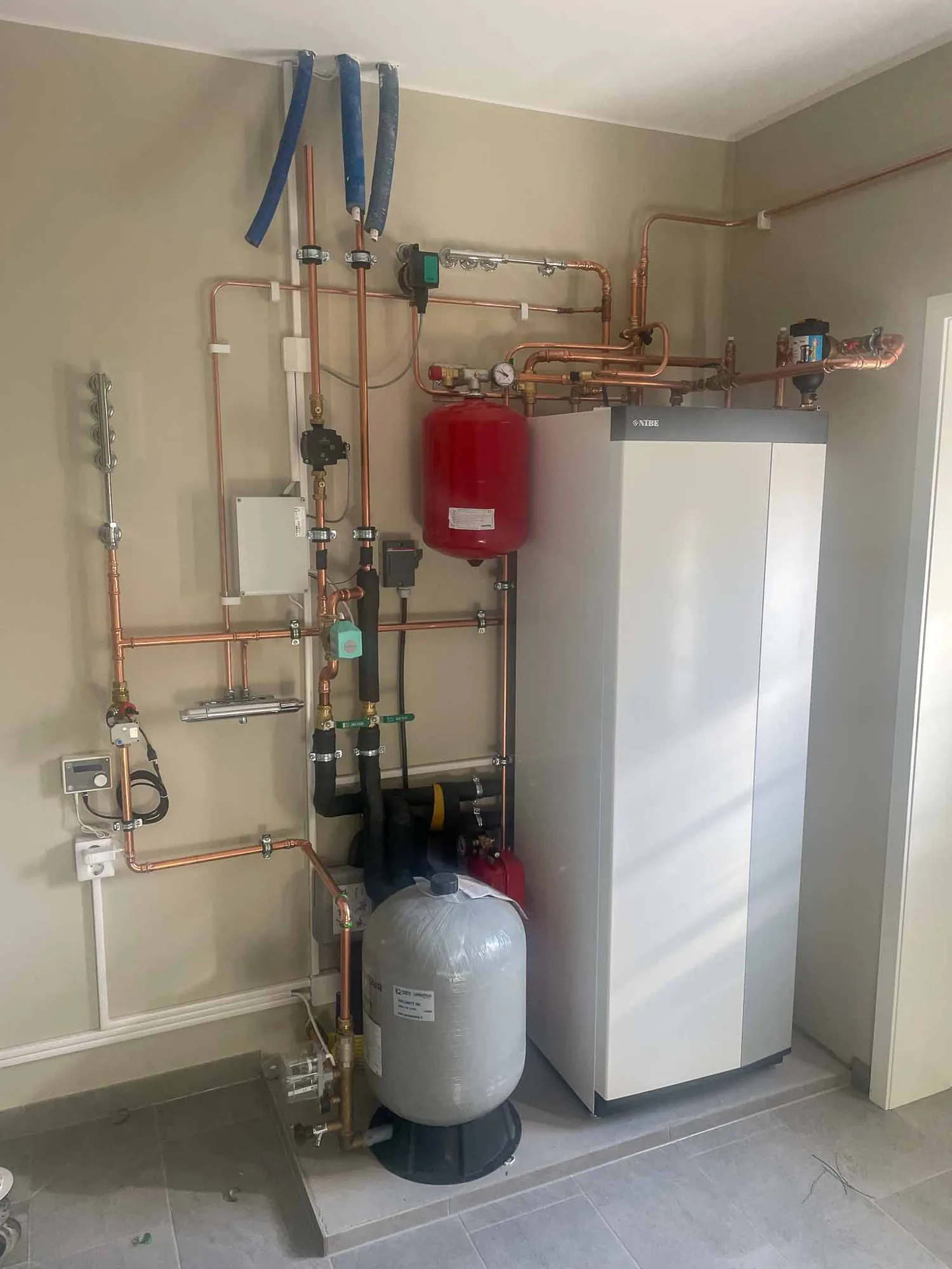 Nyinstallerad Nibe-värmepump med kopparrör, expansionskärl och varmvattenberedare i ett pannrum