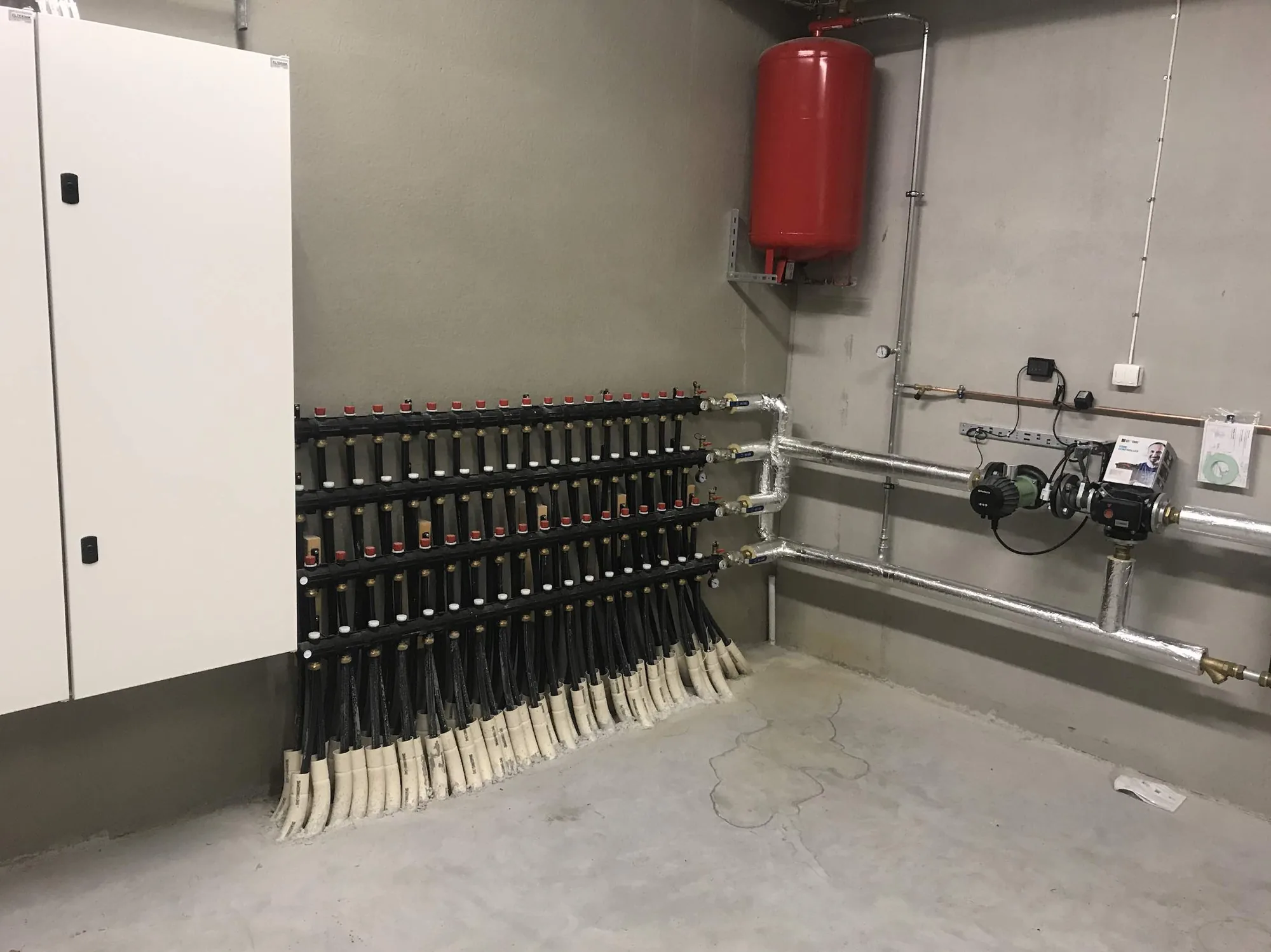 Apparatrum med golvvärmefördelare, ett rött expansionskärl och ett elskåp i ett kycklingstall
